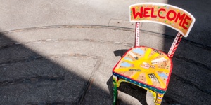 Auf einer Straße steht ein bult bemalter Holzstuhl. Auf der Rückenlehe steht »Welcome«.